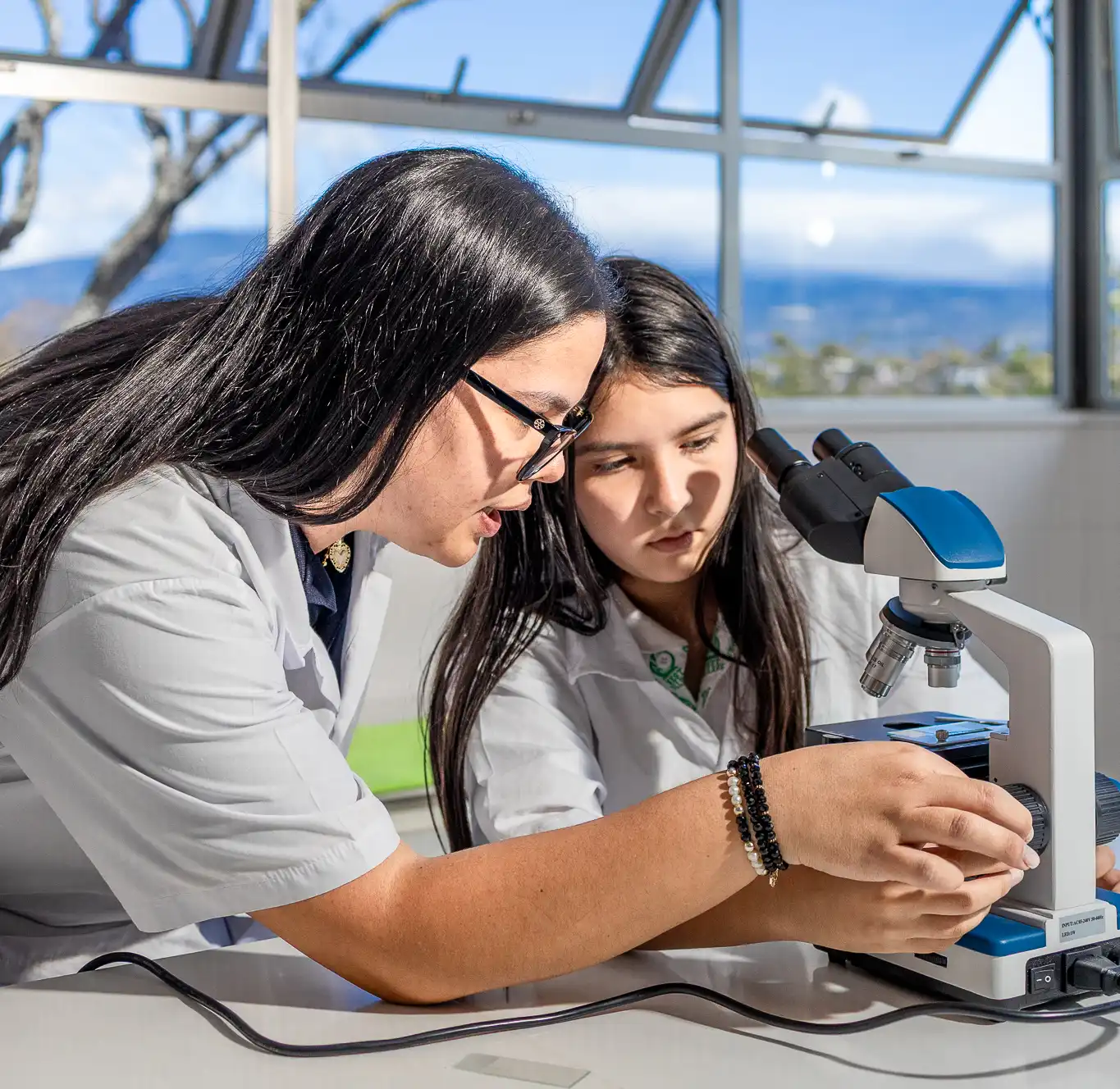 Profesora con estudiante utilizando un microscopio el laboratorio de ciencias de West College